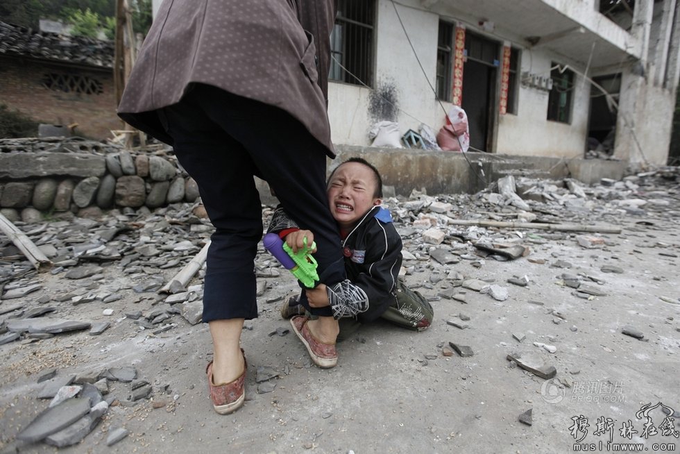 【男童抱着母亲的腿哭泣】4月21日，四川雅安芦山县，一名孩子抱着母亲的腿哭泣，背后是他们家被地震损毁的房屋。Jason Lee 摄