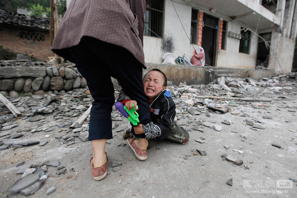 4月21日，四川雅安芦山县，一名孩子抱着母亲的腿哭泣，背后是他们家被地震损毁的房屋。Jason Lee/摄